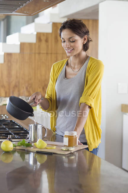 Mulher sorridente preparando chá de ervas na cozinha — Fotografia de Stock