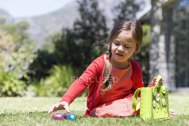Chica recogiendo huevos de Pascua en el césped en la naturaleza - foto de stock