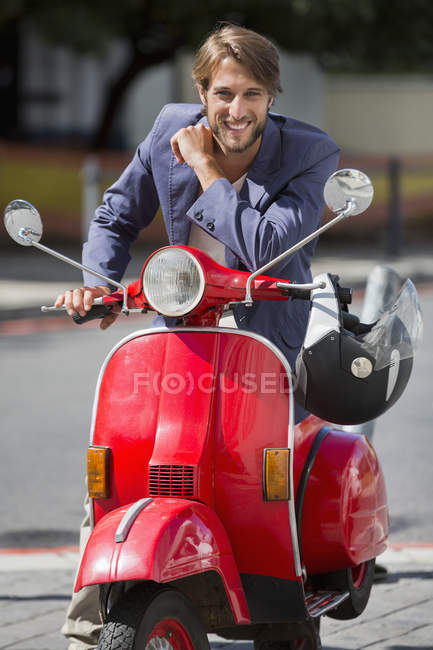 Retrato del joven sentado en scooter y sonriendo - foto de stock