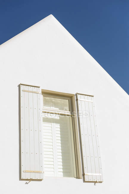 Вікно з рулонними шторами та фасадом білого будинку на тлі чистого неба — стокове фото