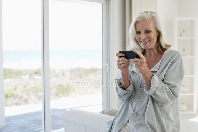 Lächelnde Frau benutzt Handy in Haus an der Küste — Stockfoto