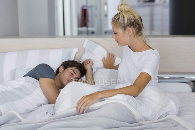 Jovem mulher olhando para o marido dormindo na cama — Fotografia de Stock