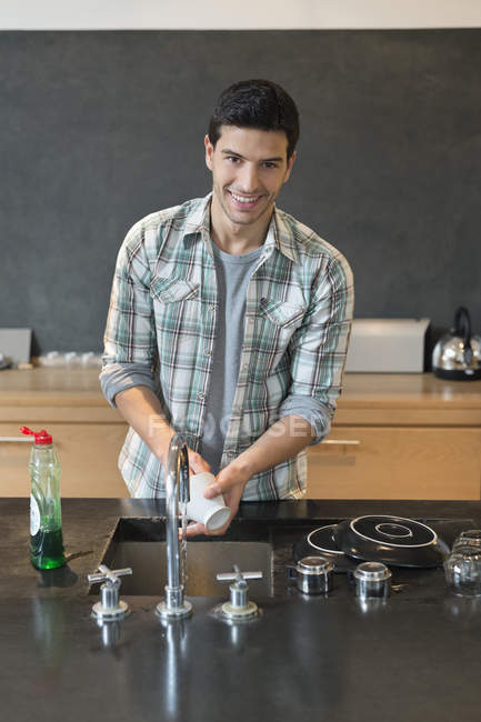 Retrato del hombre sonriente lavando platos en la cocina - foto de stock