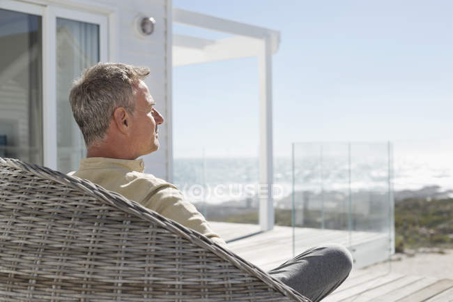 Mann entspannt sich im Korbstuhl auf der Terrasse des Hauses am Meer — Stockfoto