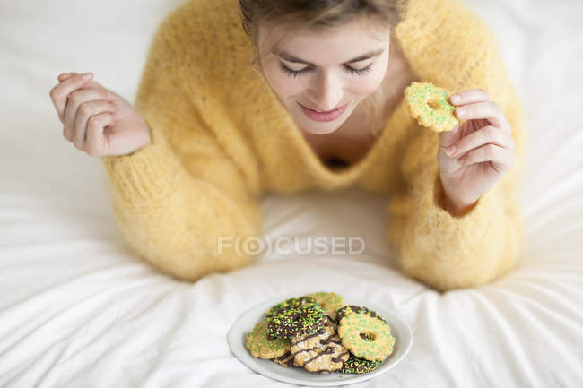 Mulher de camisola fofa amarela comendo biscoitos na cama — Fotografia de Stock