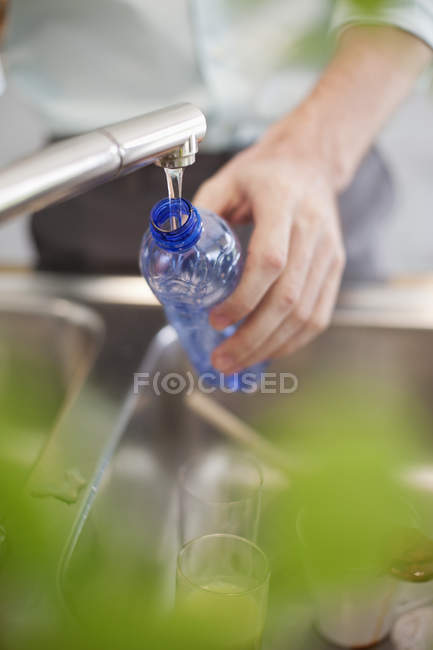 Botella de llenado de mano masculina con agua en la cocina - foto de stock