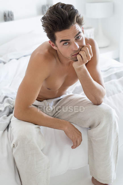 Porträt eines hemdlosen Mannes, der auf dem Bett sitzt — Stockfoto