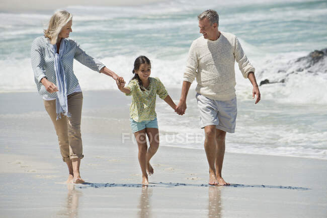 Девушка гуляет со своими бабушкой и дедушкой по пляжу — стоковое фото