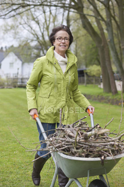 Mulher empurrando carrinho de mão cheio de ramos no jardim — Fotografia de Stock
