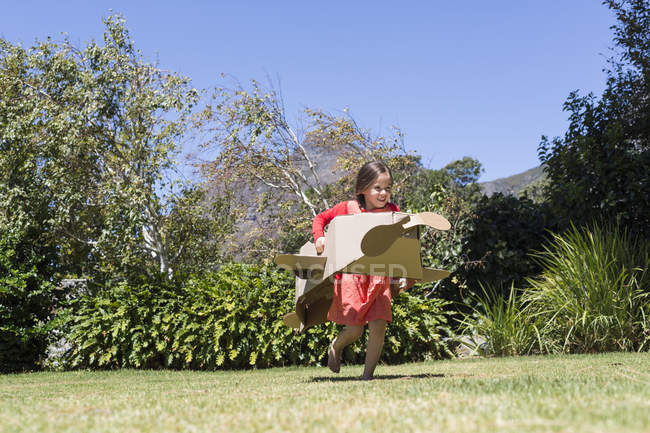 Маленькая девочка играет с картонным самолетом на газоне — стоковое фото
