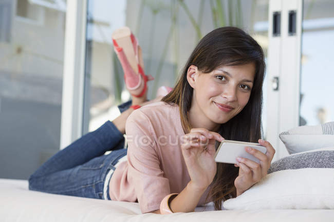 Portrait of smiling woman lying on bed and using mobile phone — Stock Photo