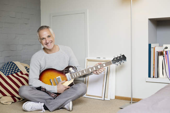 Retrato de um homem feliz tocando guitarra em casa — Fotografia de Stock