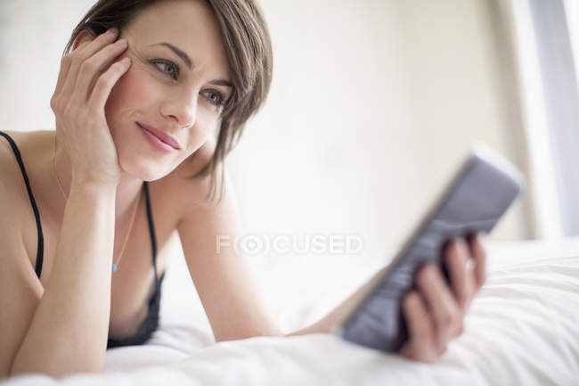 Smiling woman lying on bed and using mobile phone — Stock Photo