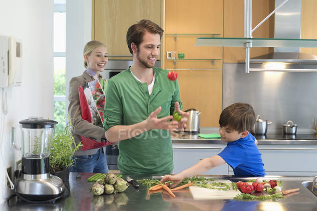 Родители смотрят, как сын режет овощи на кухне — стоковое фото