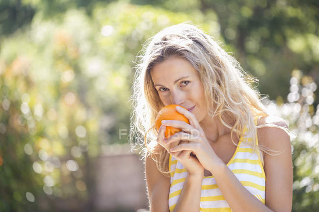 Portrait of woman holding orange fruit in sunny garden — Stock Photo