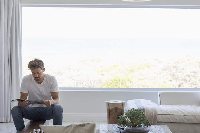 Junger Mann liest zu Hause im Wohnzimmer Magazin — Stockfoto