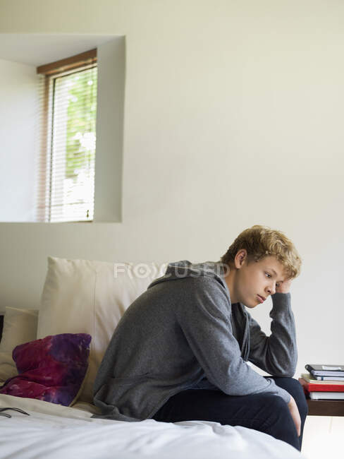 Мальчик-подросток сидит на кровати и думает: — стоковое фото
