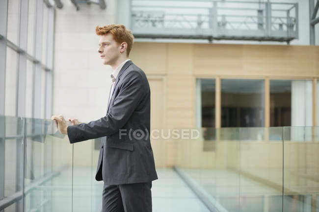 Бизнесмен смотрит через стеклянное окно в офисном коридоре — стоковое фото