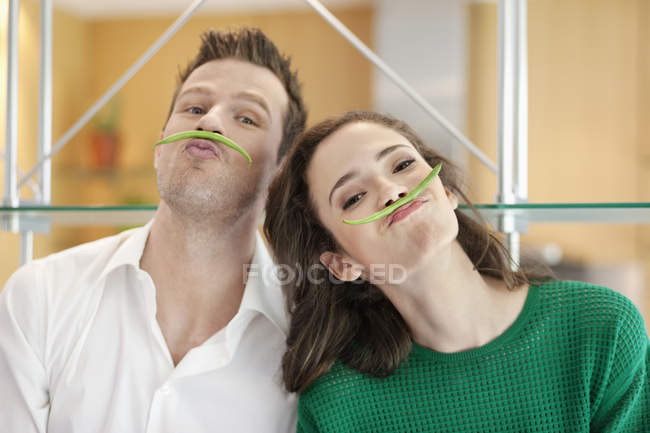 Портрет пары, играющей с зеленой фасолью на кухне — стоковое фото
