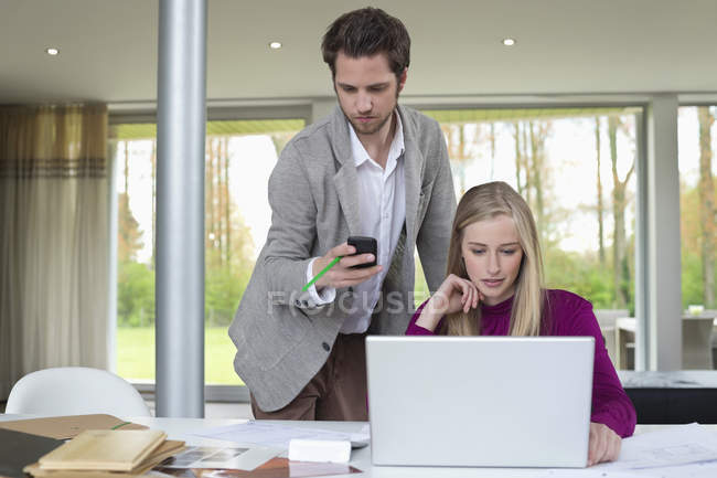 Женщина работает на ноутбуке с мужчиной с помощью мобильного телефона в офисе — стоковое фото