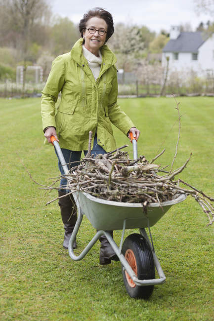 Donna spingendo carriola piena di rami in giardino — Foto stock
