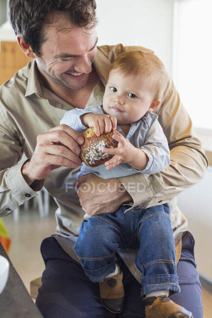 Un homme donne du pain à son fils à un comptoir de cuisine — Photo de stock