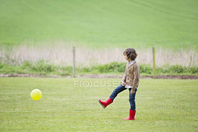 Хлопчик грає з м'ячем у зеленому осінньому полі — стокове фото