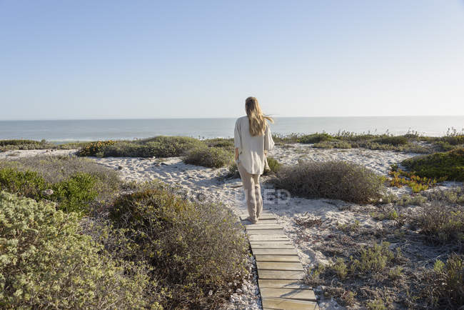 Vista trasera de la mujer caminando por el camino de madera en la costa - foto de stock