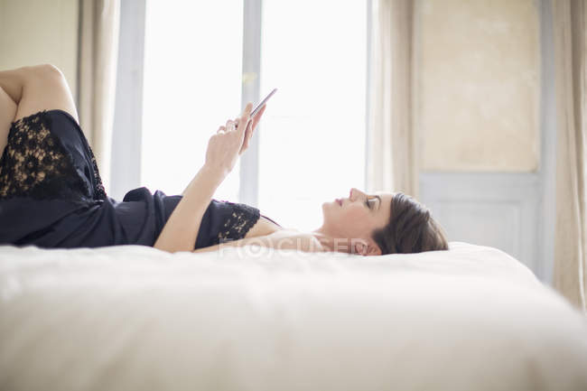 Elegant woman lying on bed and using a mobile phone — Stock Photo