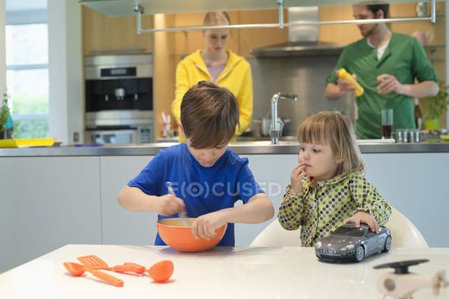 Маленька дівчинка з іграшковою машиною дивиться на брата, який готує на кухні — стокове фото