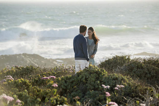 Casal em pé na vegetação na costa do mar e olhando uns para os outros — Fotografia de Stock