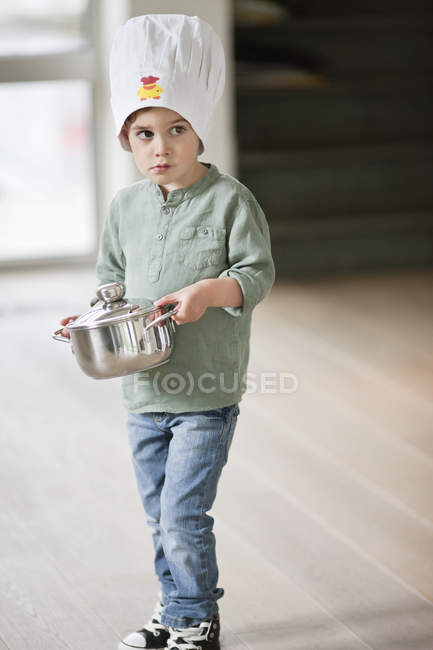 Garçon en chapeau de chef portant une casserole et regardant loin — Photo de stock