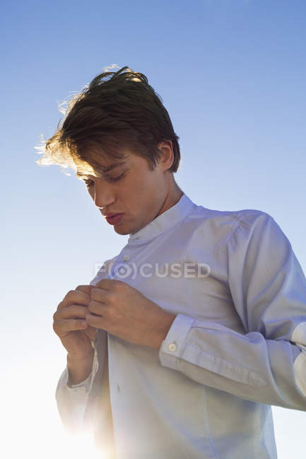 Man buttoning white shirt in front of blue sky — Stock Photo