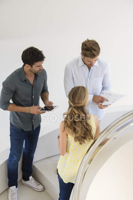 Three business friends standing on staircase looking at document — Stock Photo