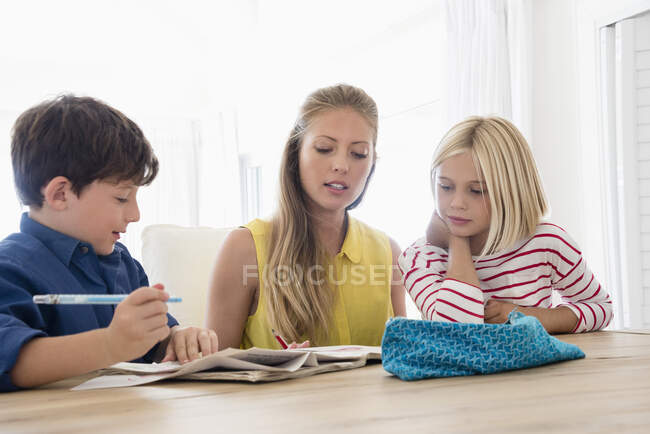 Madre e hijos haciendo la tarea en la mesa - foto de stock