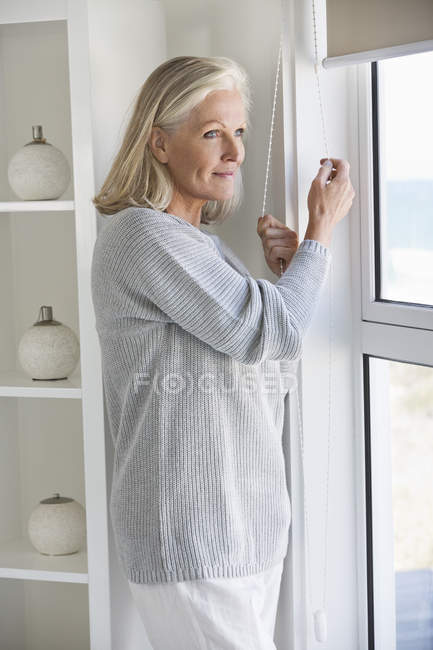 Senior woman looking through window at home — Stock Photo