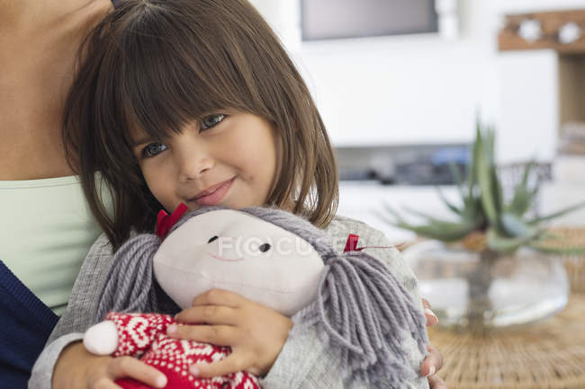 Close-up of little girl sitting with mother and holding rag doll — Stock Photo