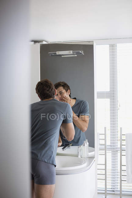 Young checking face in mirror in bathroom — Stock Photo