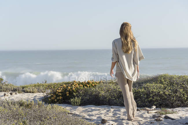 Vista trasera de la mujer de pie en la playa y mirando a la vista - foto de stock