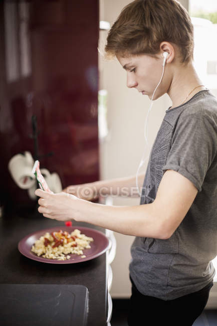 Teenage boy listening to music with earphones and making lunch — Stock Photo