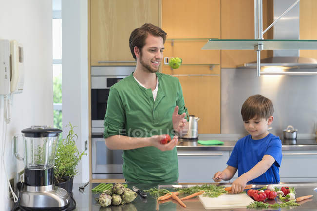 Hombre e hijo cortando verduras en la cocina - foto de stock