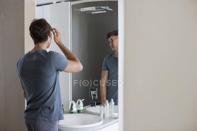 Jeune homme vérifier les cheveux dans le miroir dans la salle de bain — Photo de stock
