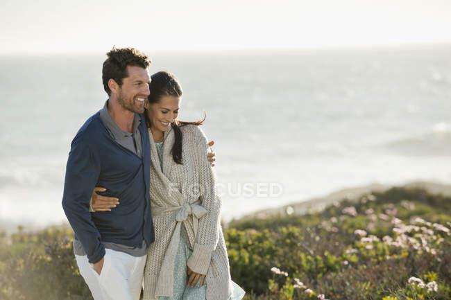 Sorrindo casal abraçando andando na costa do mar — Fotografia de Stock