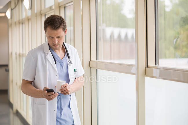 Male doctor messaging with mobile phone while drinking coffee — Stock Photo
