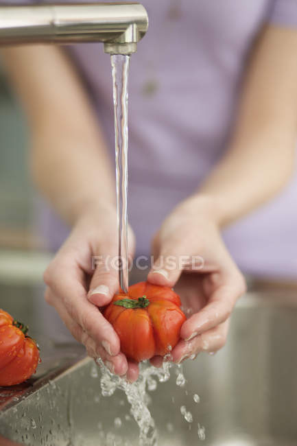 Primer plano de la mujer lavando tomates en fregadero en la cocina - foto de stock