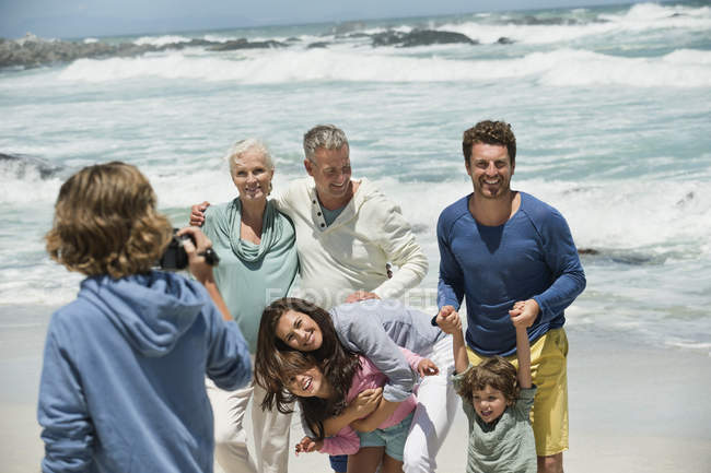 Мальчик фотографирует семью, стоящую на песчаном пляже — стоковое фото