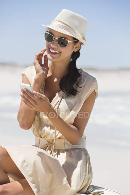 Sorrindo mulher elegante usando telefone celular na praia — Fotografia de Stock