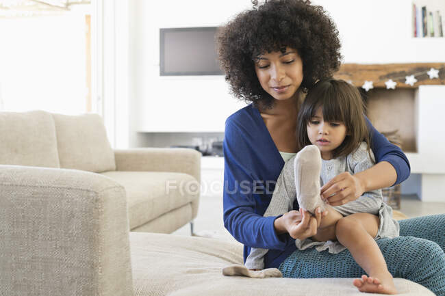 Mulher vestindo meias para sua filha e sorrindo — Fotografia de Stock