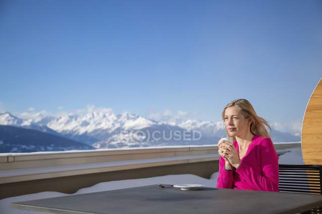 Женщина пьет кофе на террасе с видом на горы, Кранс-Монтана, Швейцарские Альпы, Швейцария — стоковое фото