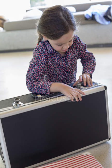 Маленькая девочка пытается закрыть чемодан дома — стоковое фото